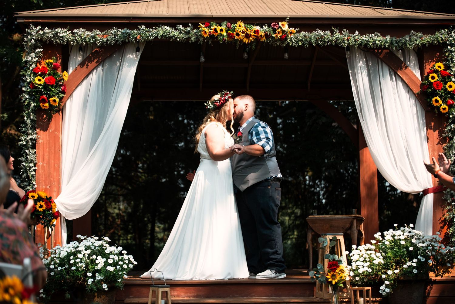 A couple shares their first dance under a rustic outdoor wedding arch decorated with flowers.
