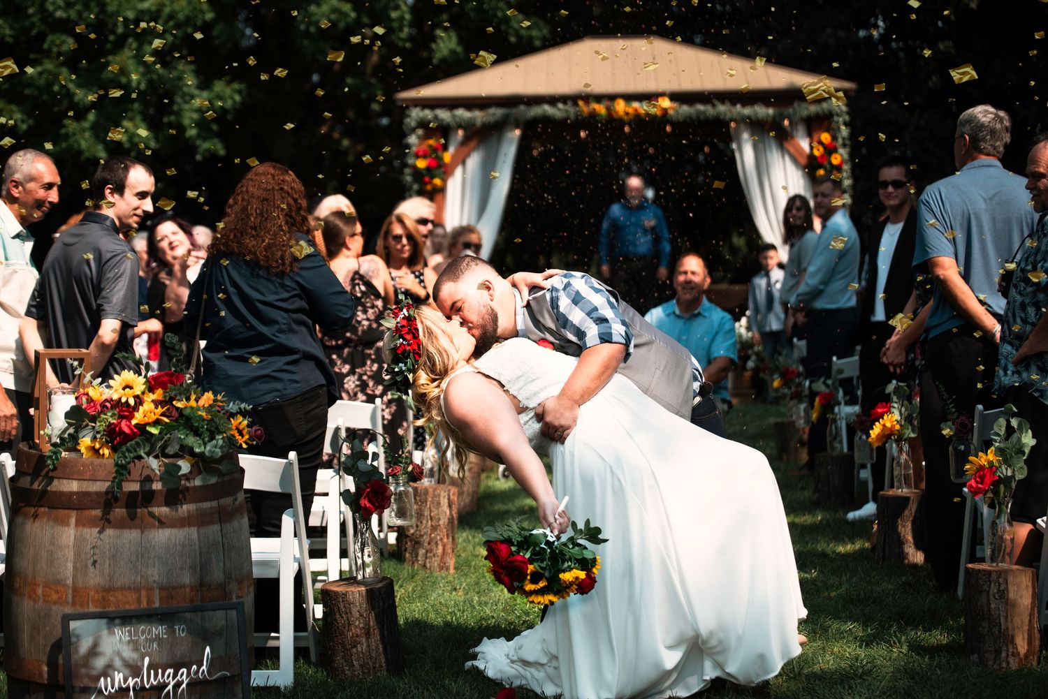 An outdoor wedding ceremony in a garden setting with rustic wooden barrels and floral decorations.