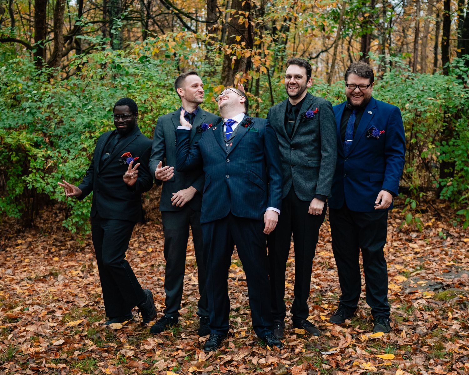 Wedding party members laugh together during outdoor fall photo session in the woods.