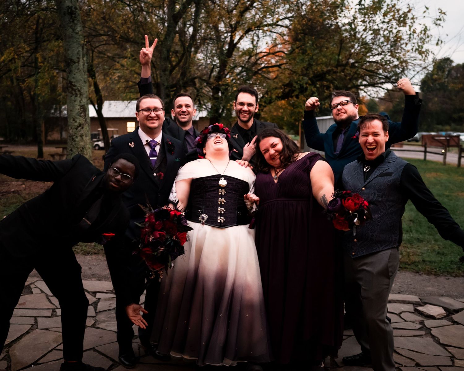 Wedding party poses together outdoors during fall season with autumn foliage in background.