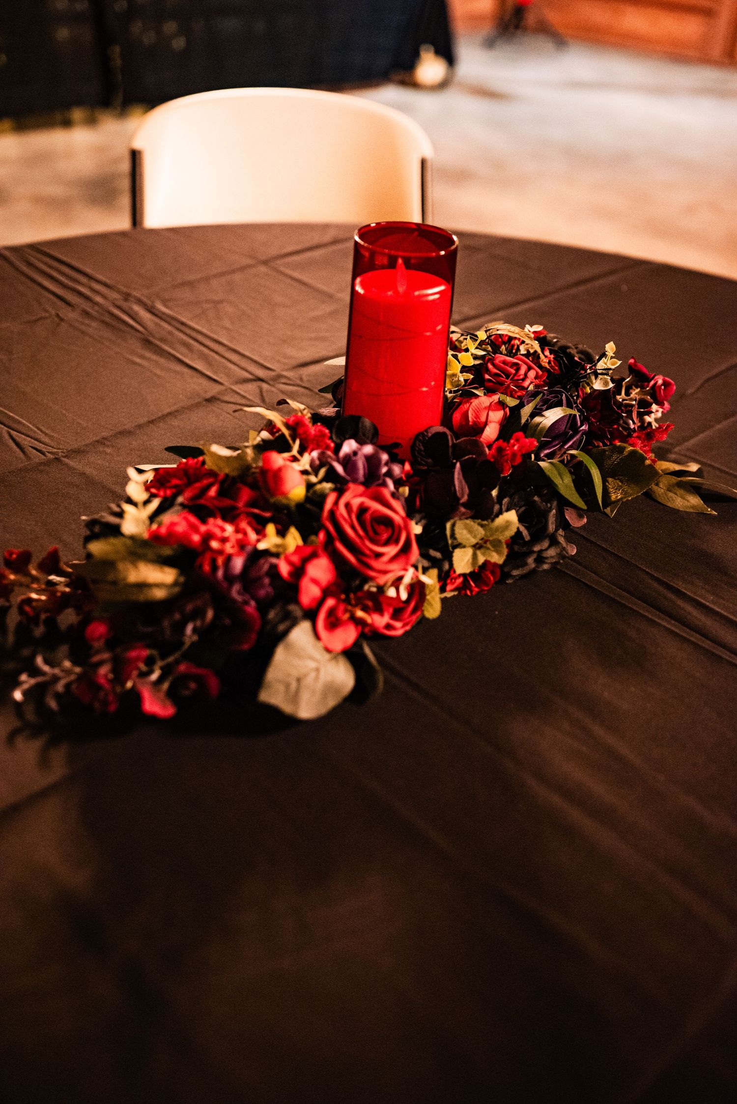 Elegant table decor with red roses and candles on black tablecloth for gothic wedding theme.