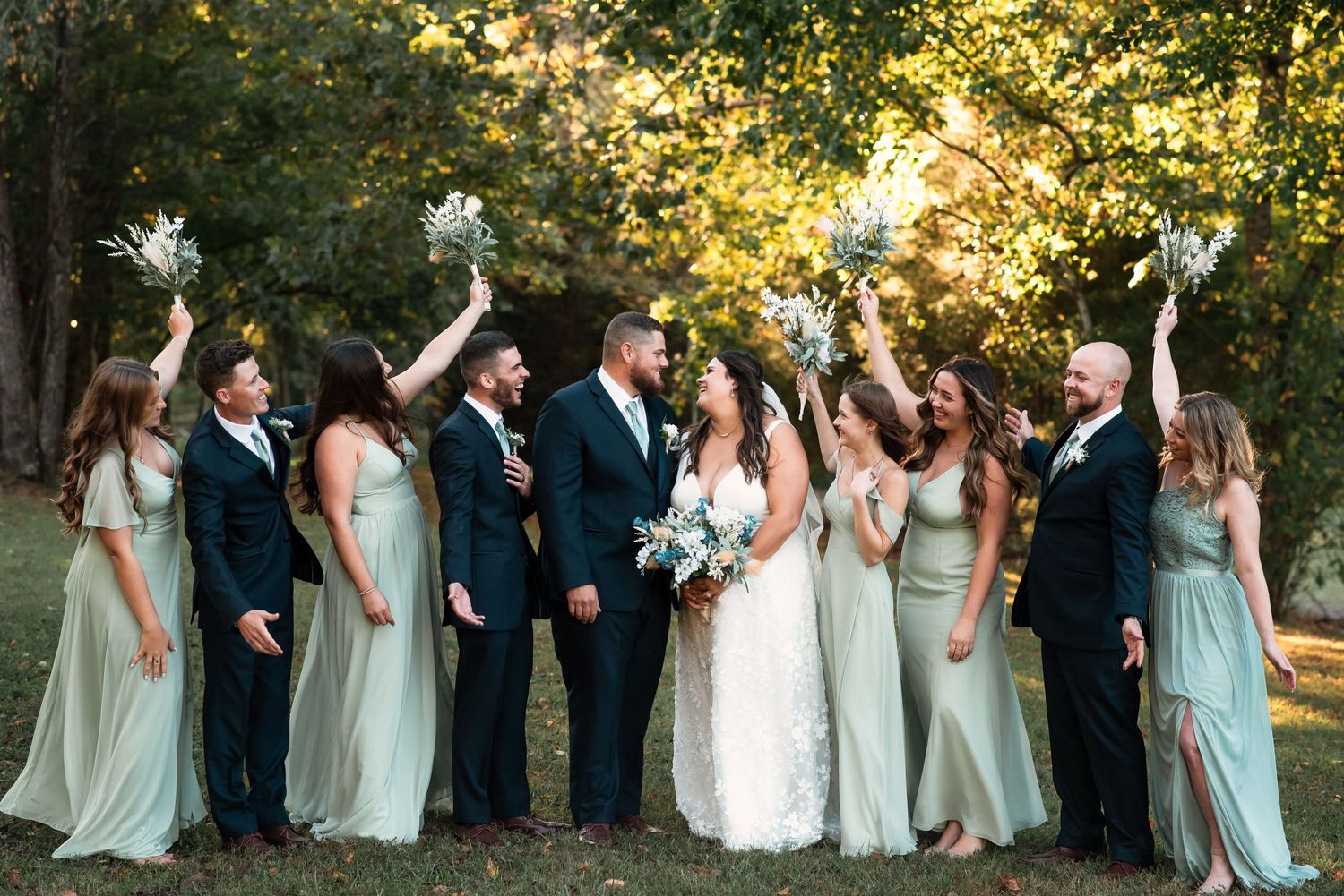 Wedding party lined up outdoors with bridesmaids in mint dresses and groomsmen in dark suits.