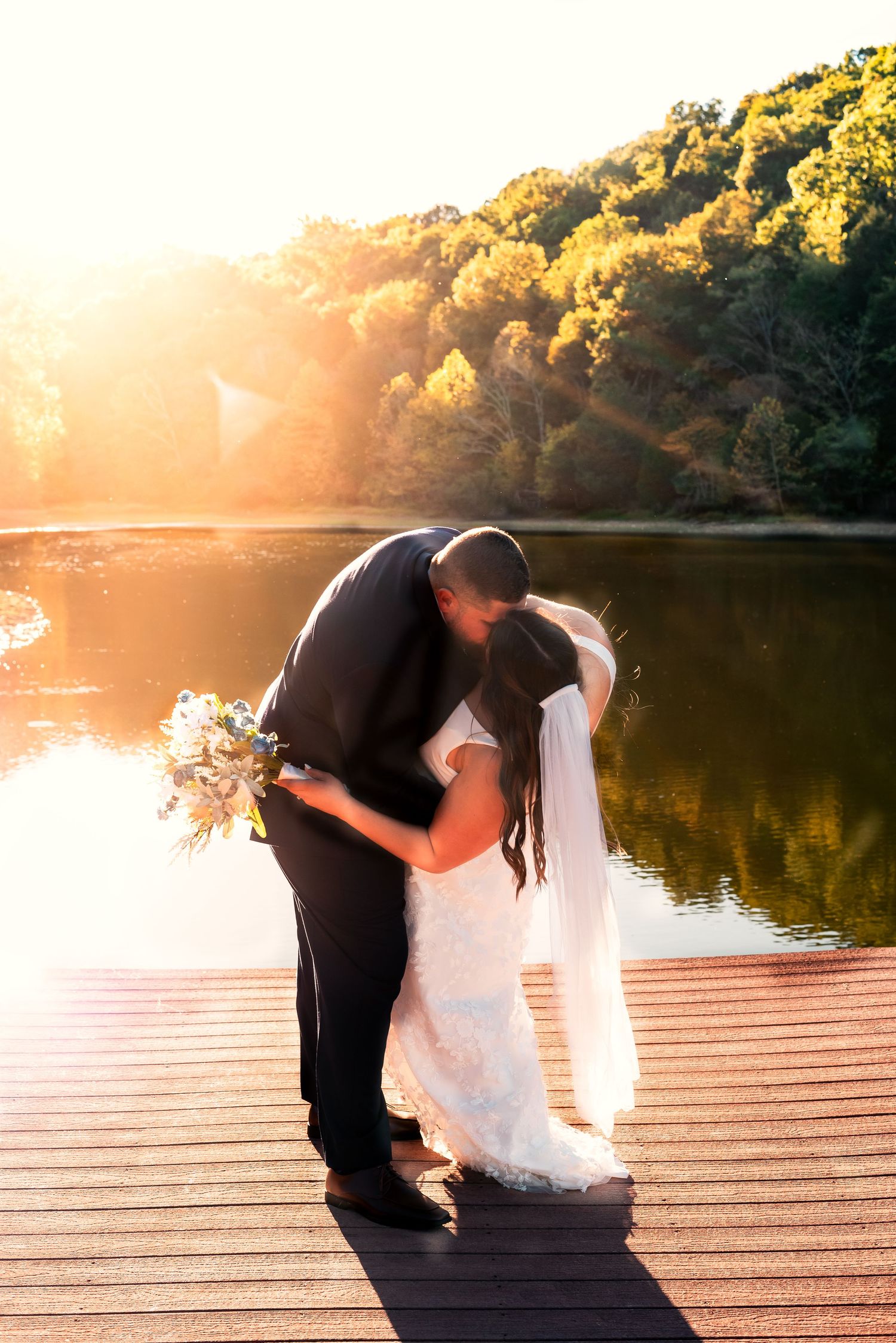 Silhouetted couple in wedding attire dancing on a wooden pier at sunset.