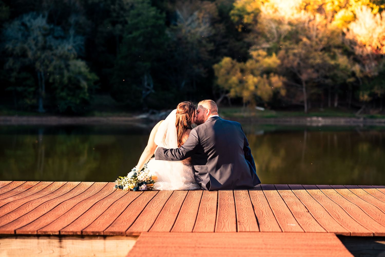Newlyweds share an intimate moment on a lakeside dock during golden hour.