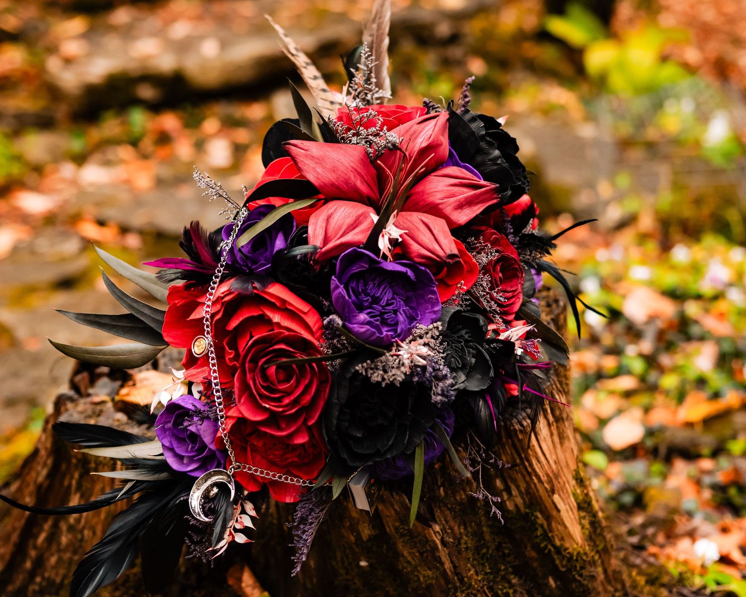 Dramatic floral arrangement with red roses and purple flowers on autumn foliage.