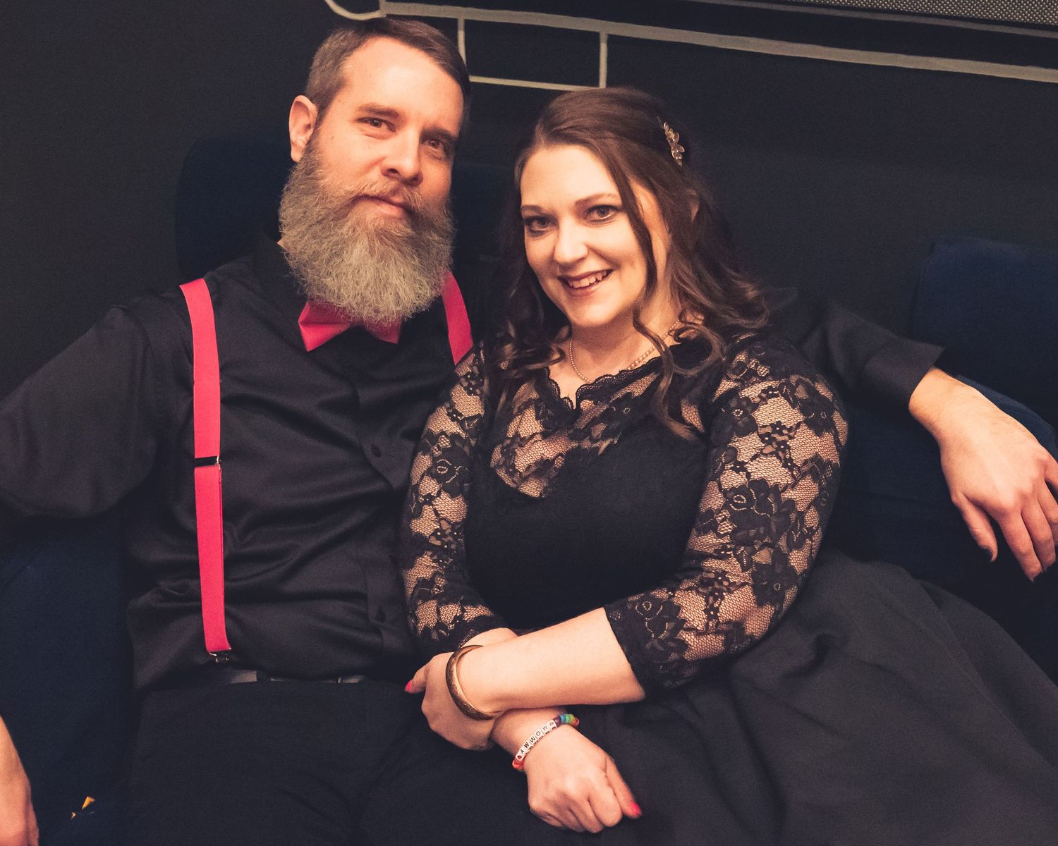 Intimate couple portrait session with black lace dress and pink accents against dark background.