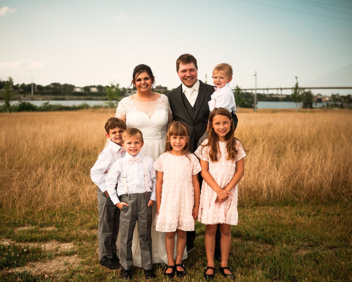 Wedding party stands together in a golden field at sunset wearing pink and black formal attire.