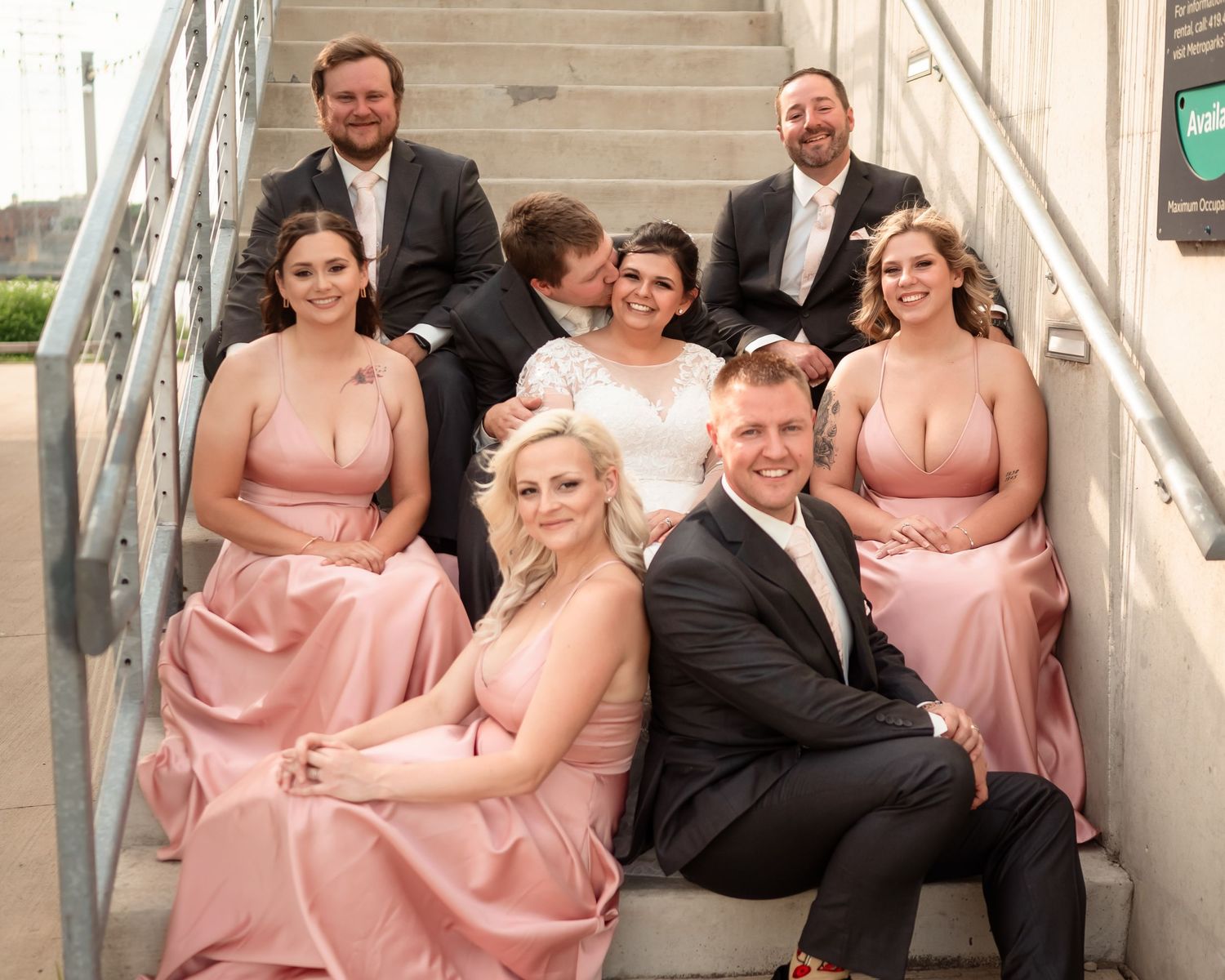 Wedding party poses on concrete stairs wearing pink bridesmaid dresses and black suits.