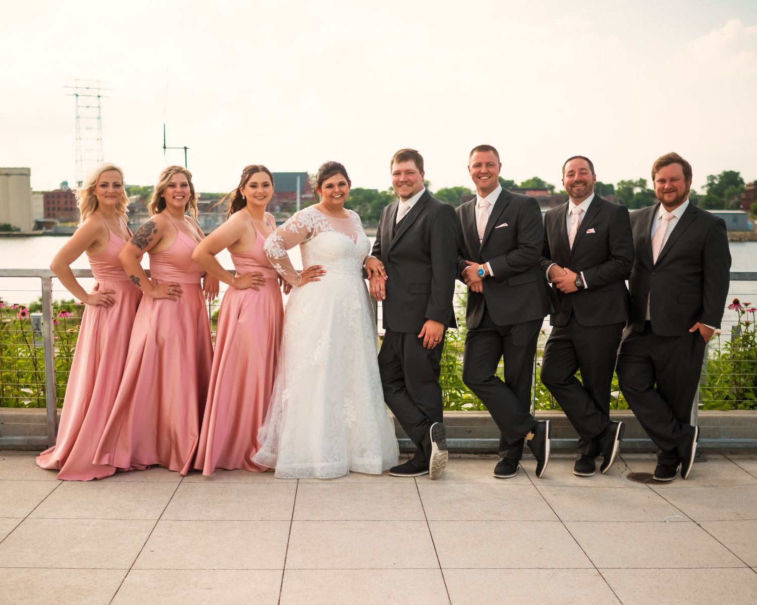 Wedding party arranged in formal line on outdoor terrace wearing pink dresses and black suits.