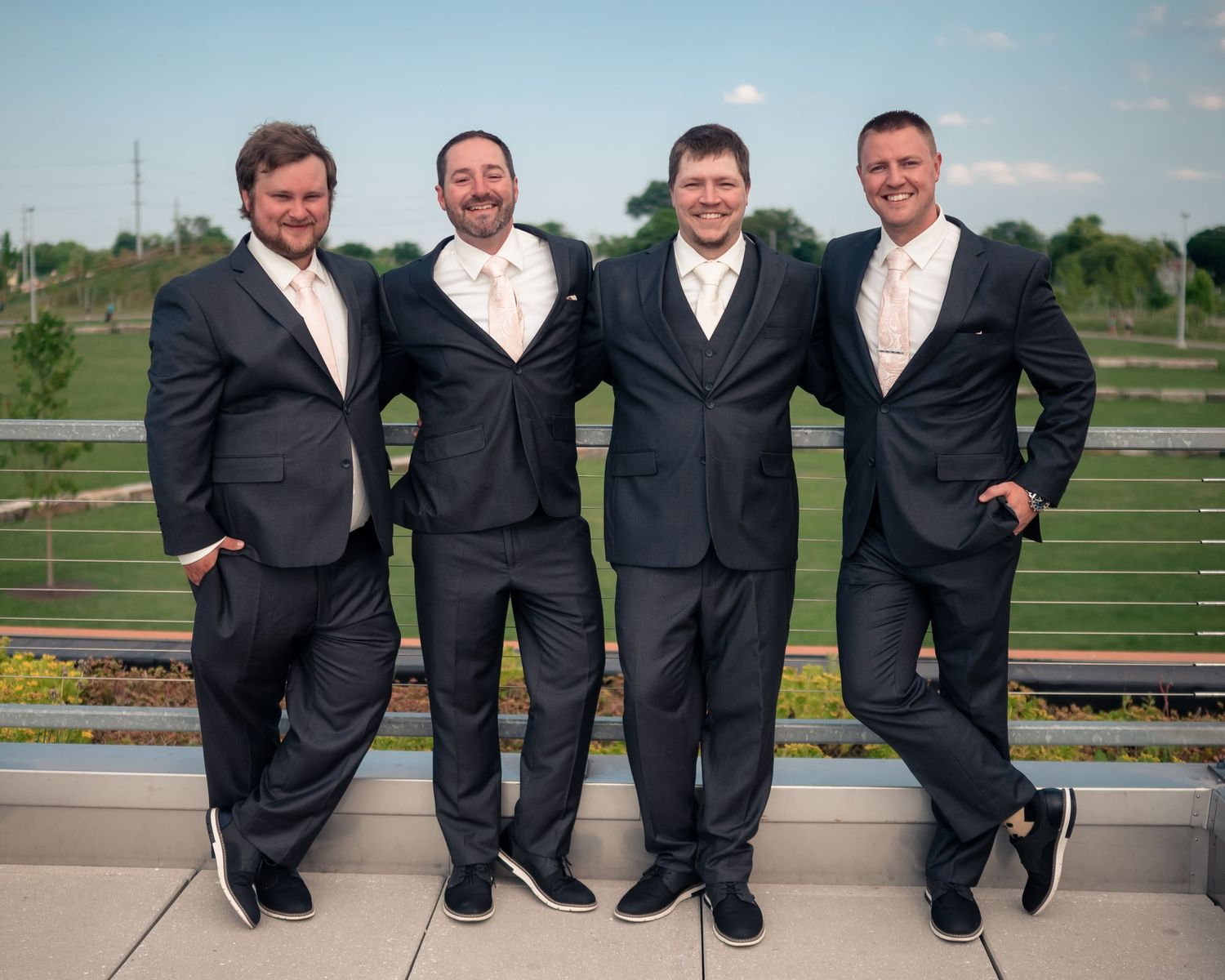 Groomsmen in black suits pose casually on outdoor patio.