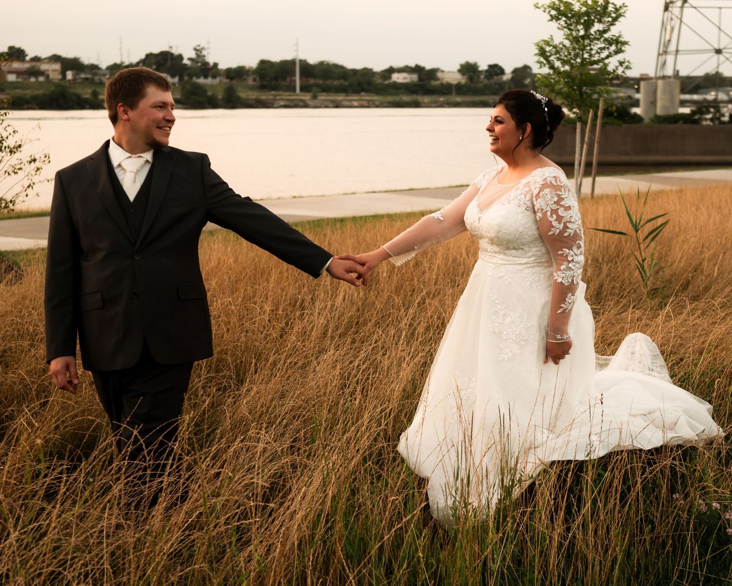 Couple walks through tall grass field during sunset wedding photoshoot.