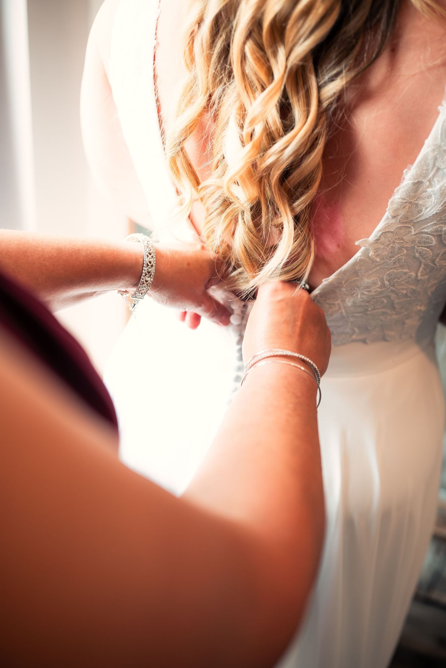 Close-up of hands styling blonde curled hair with jewelry details.