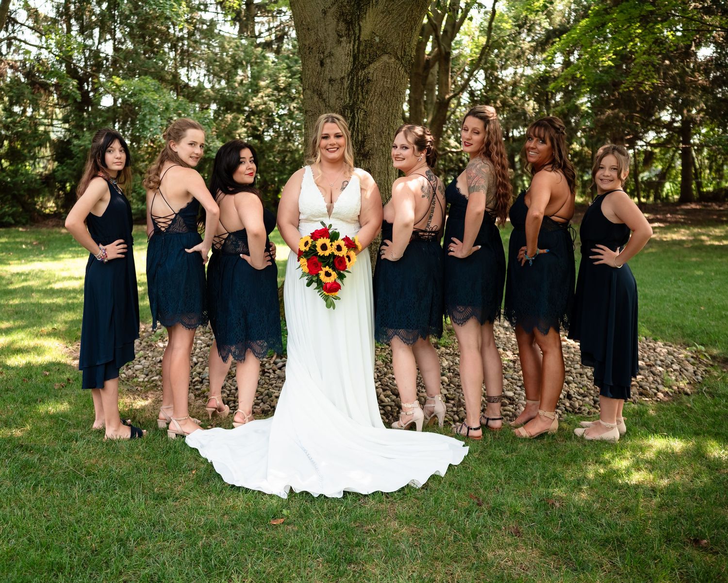Bridal party posing outdoors with navy blue bridesmaid dresses and sunlit garden backdrop.