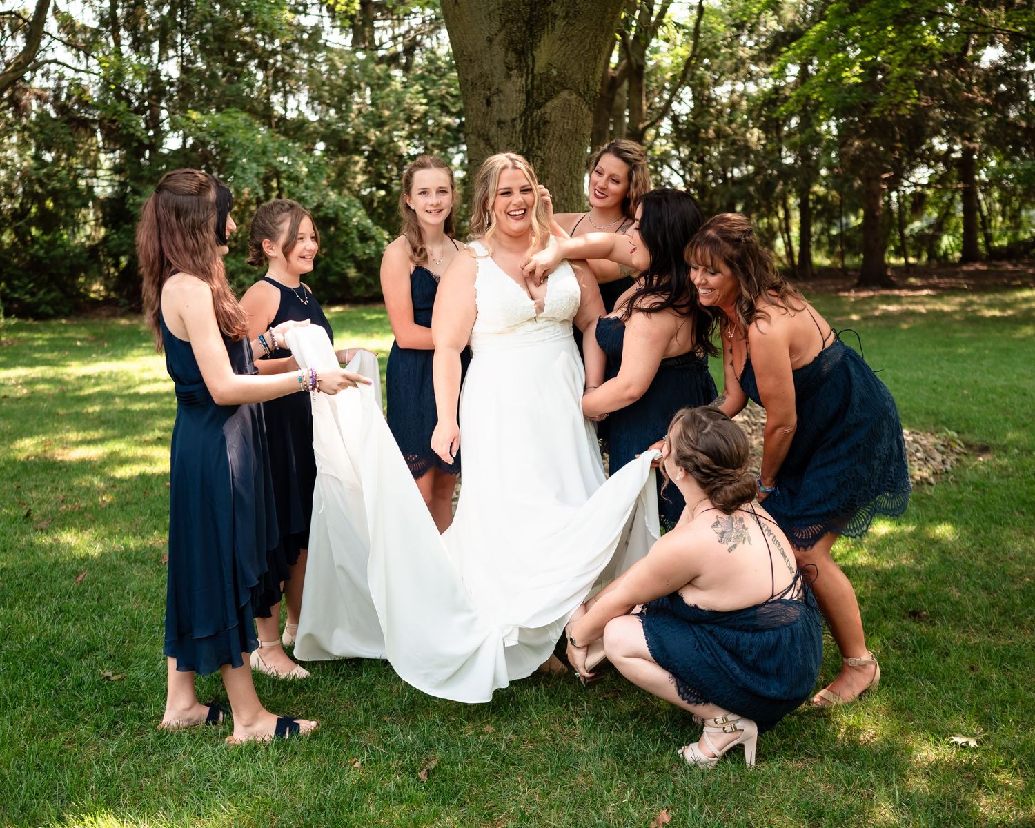 Wedding party having fun while adjusting the bride's dress outdoors.