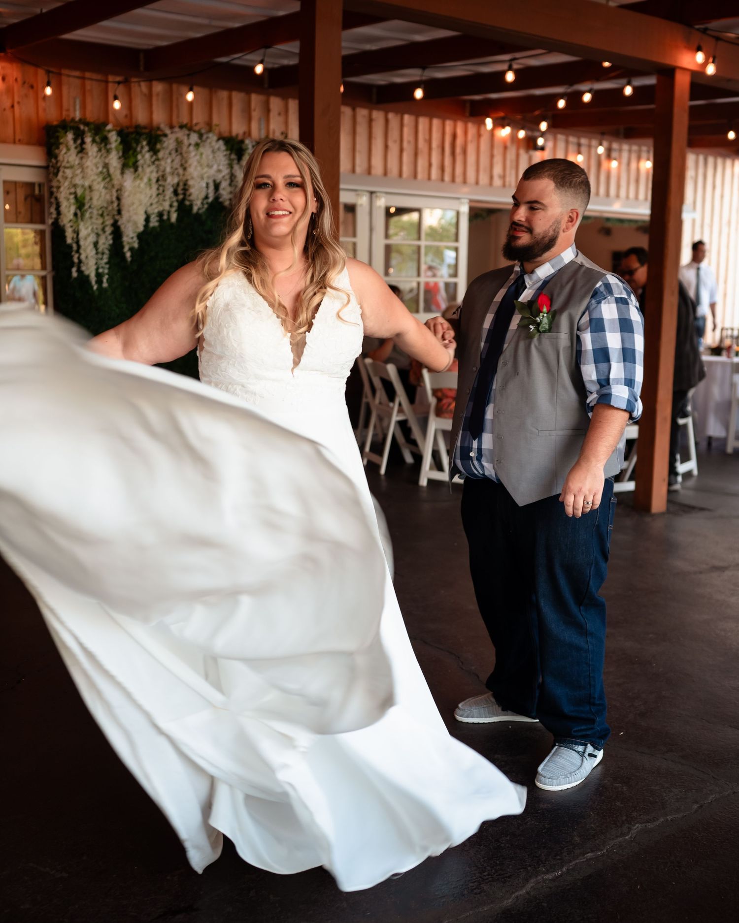 A couple performs a playful dance move during their wedding reception under string lights.