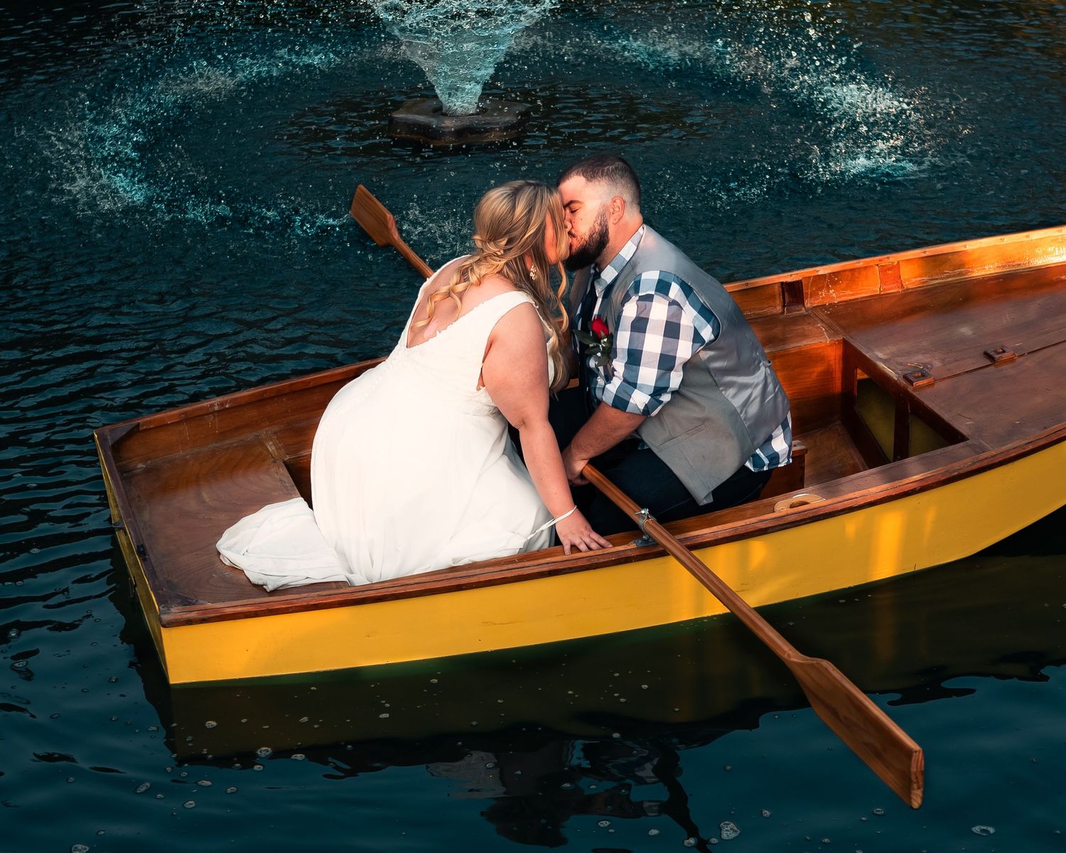 A couple rides in a wooden rowboat on dark waters during their wedding photoshoot.