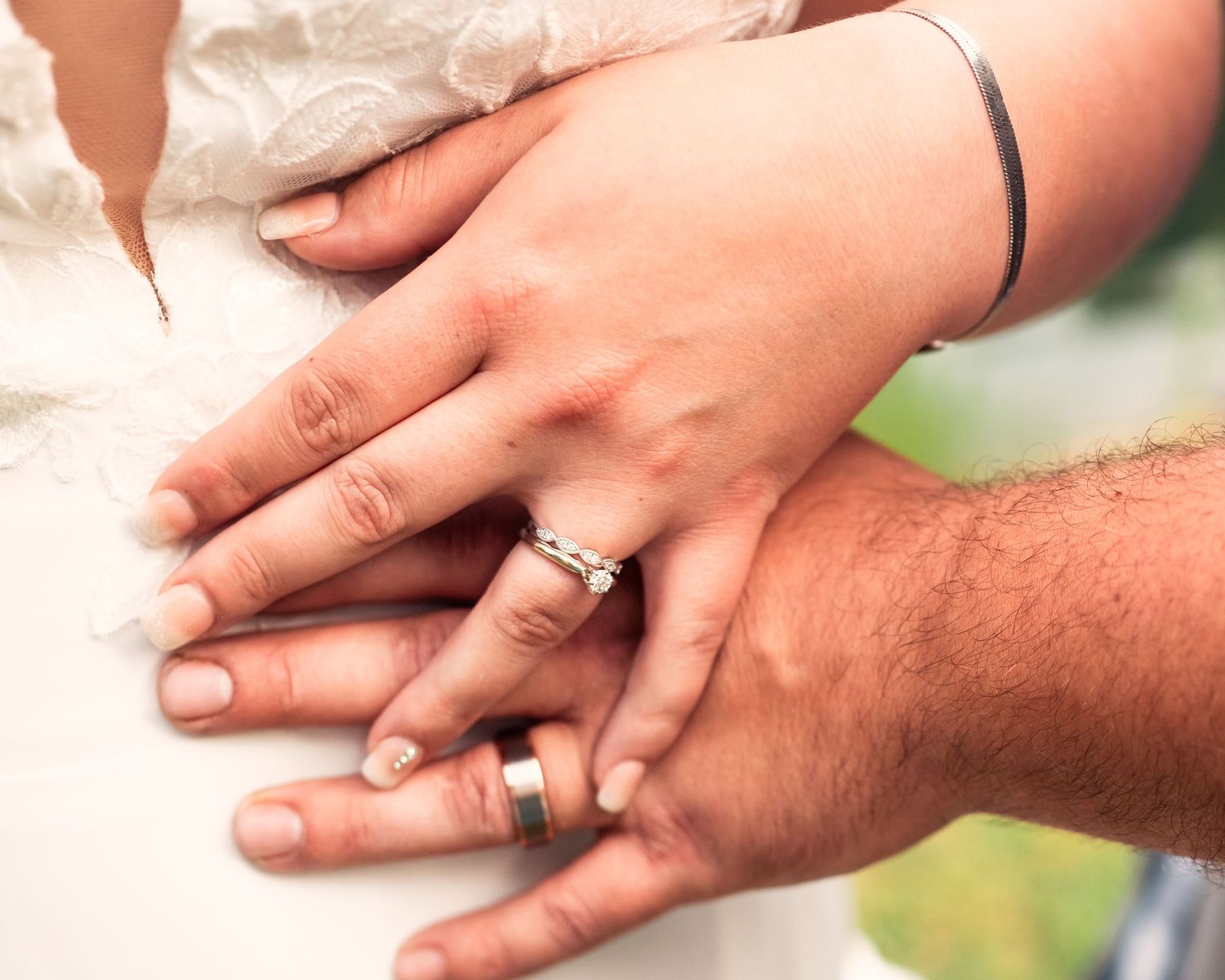 Close-up shot of hands with wedding rings intertwined on a white surface.