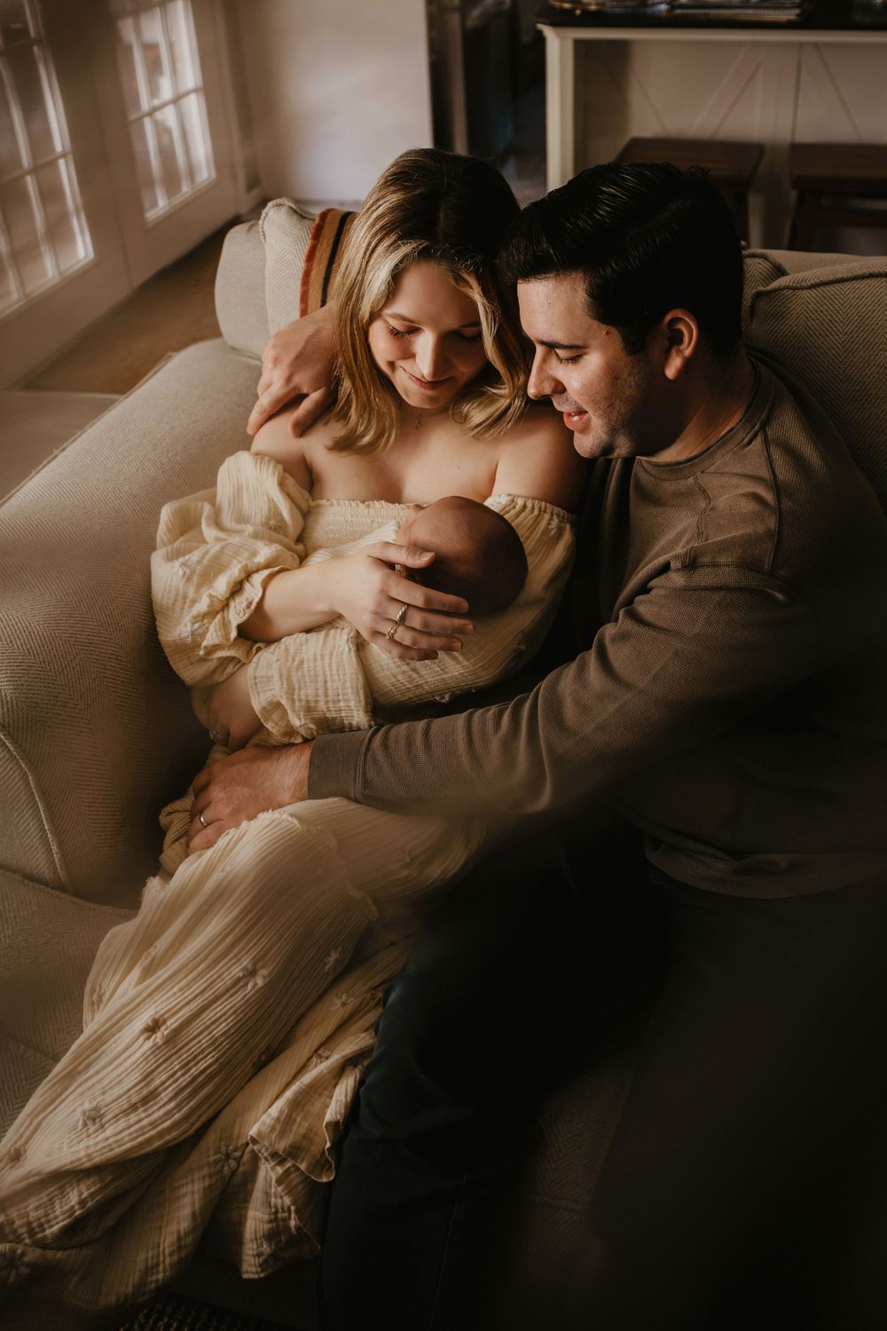 Romantic couple in warm lighting share intimate moments on couch in sequence of moody indoor newborn photographs.