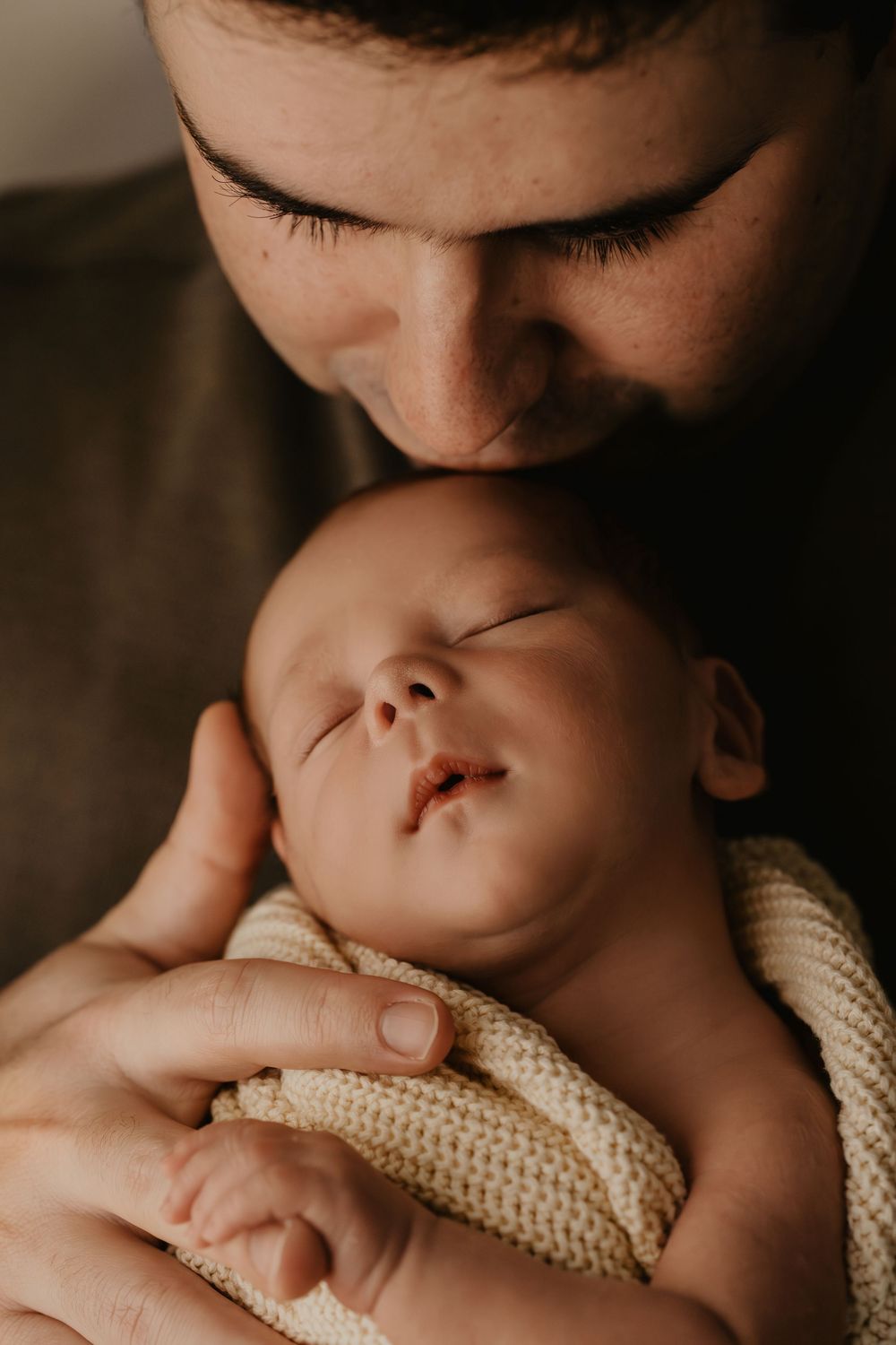Close-up macro shots of baby being held by his father, focusing on nose and lips in warm tones with a cream-colored knit blanket.