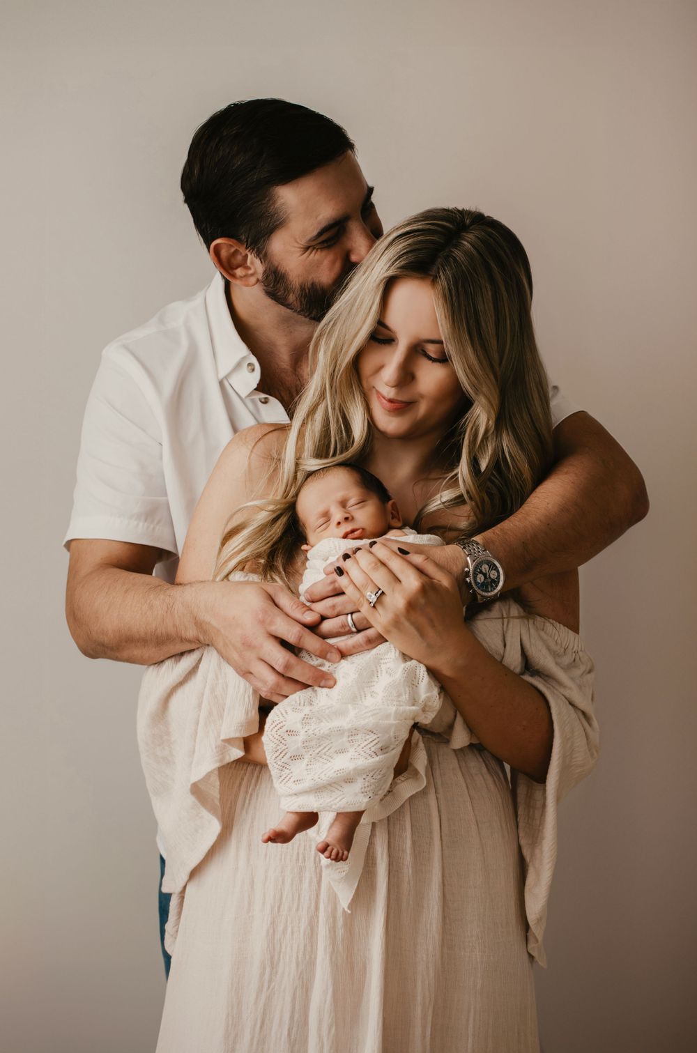 Intimate family portrait with newborn baby in neutral studio setting.