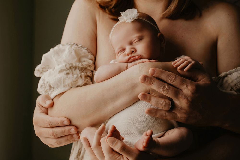 A sleeping newborn baby swaddled in soft white fabric is gently cradled in caring mom's arms.