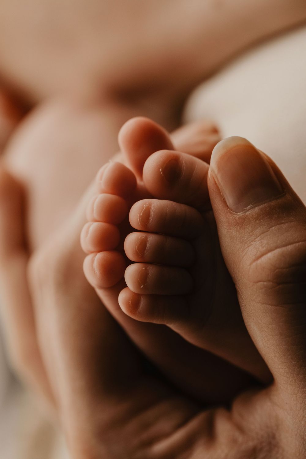 Close-up macro photograph of tiny newborn baby toes in soft warm lighting against neutral background.