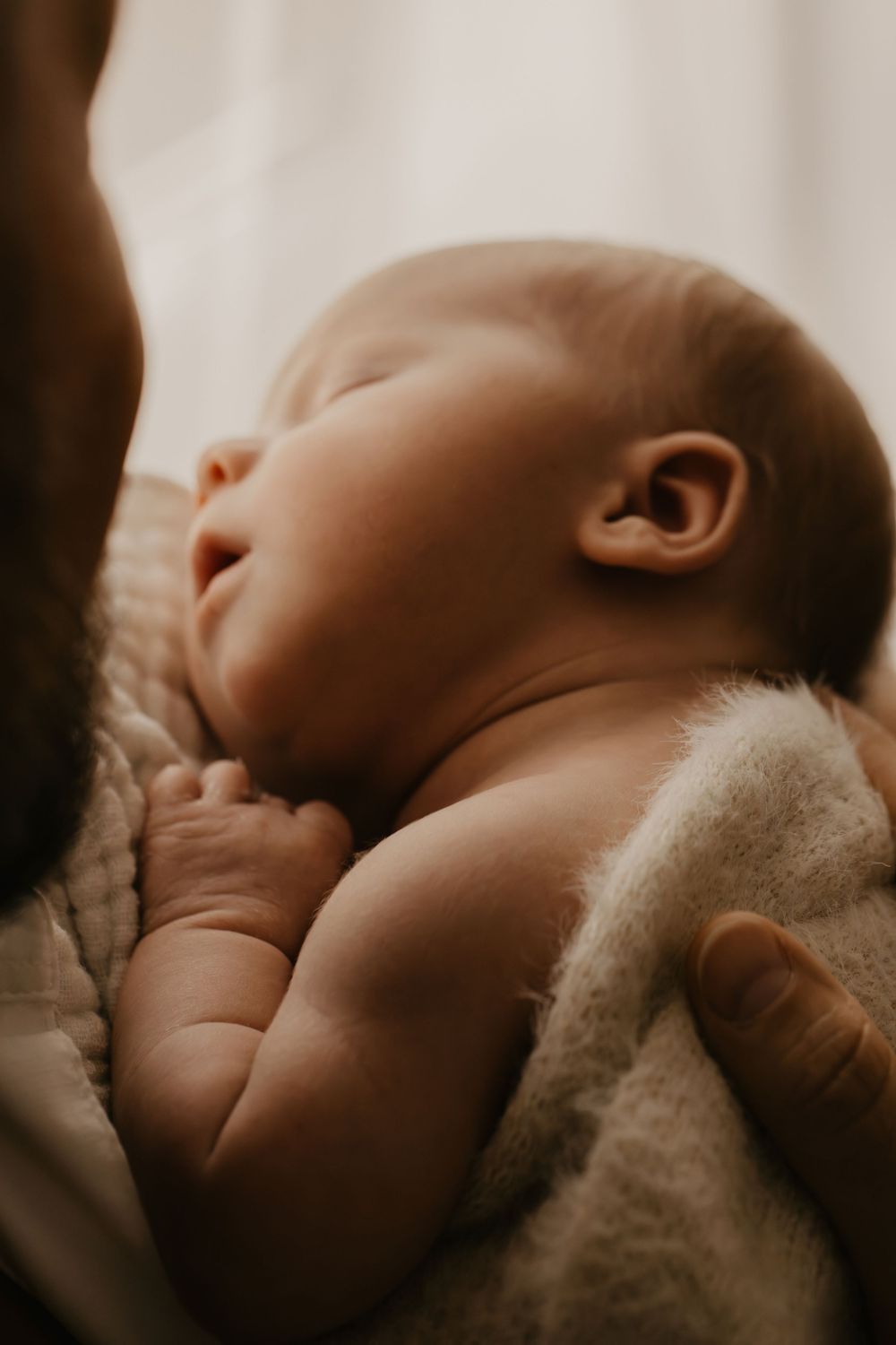 Close-up sequence of a sleeping newborn baby nestled in soft beige blankets with dramatic lighting.