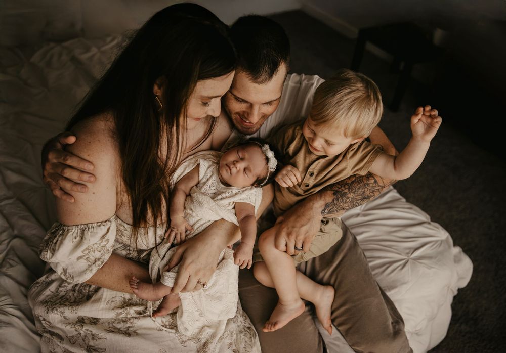 Family sharing joyful laughter together while embracing their newborn on bed in warm natural lighting.