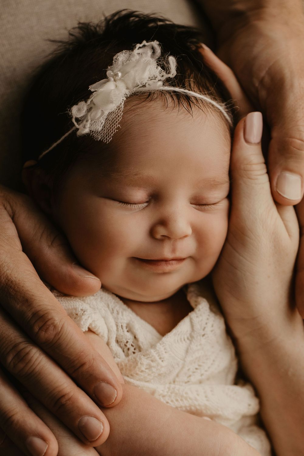 Sepia-toned newborn photography series showing a sleeping baby in white lace with gentle hands cradling their face.