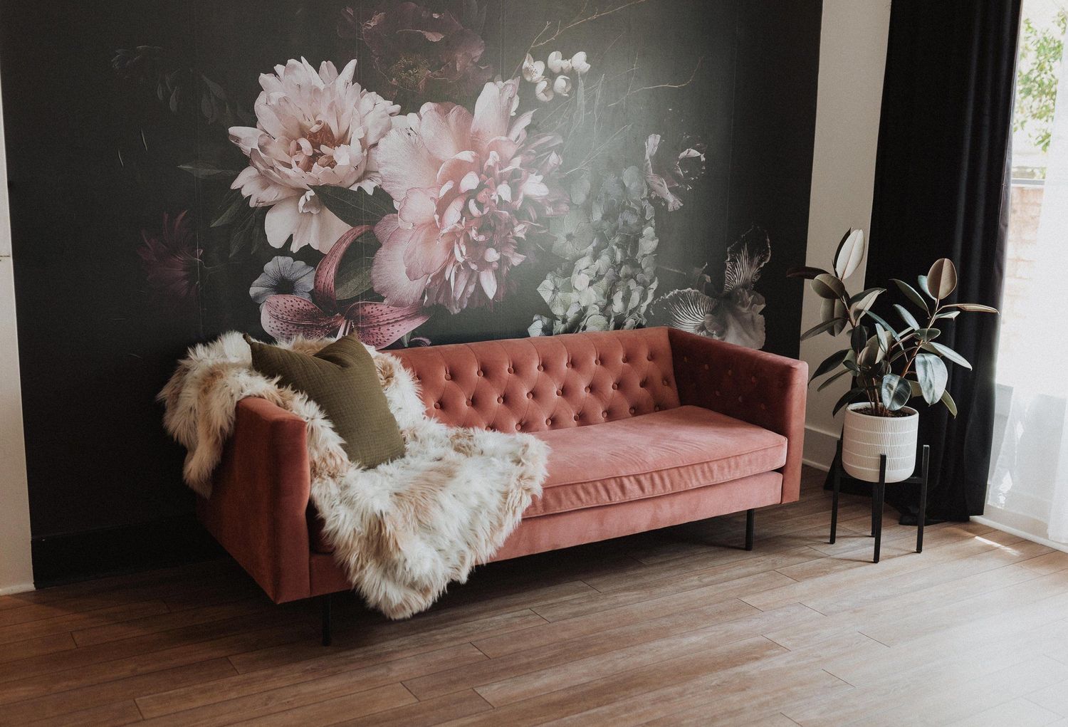 Pink velvet sofa with floral wall mural and sheepskin throw.