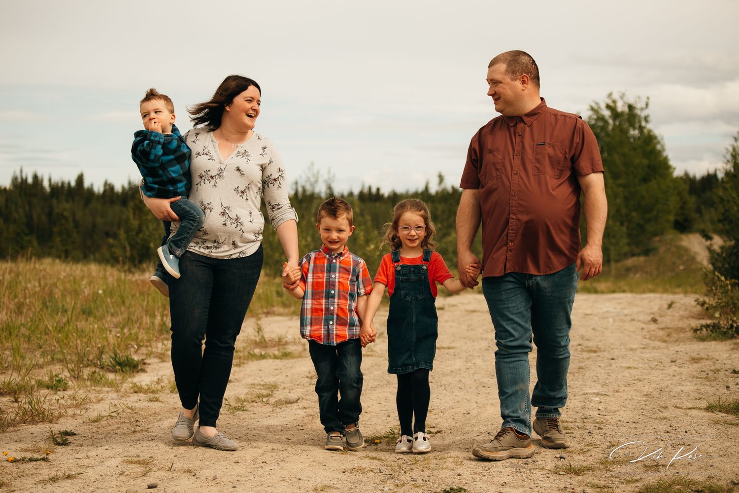 Happy family of five walking together on a dirt path in an open field.