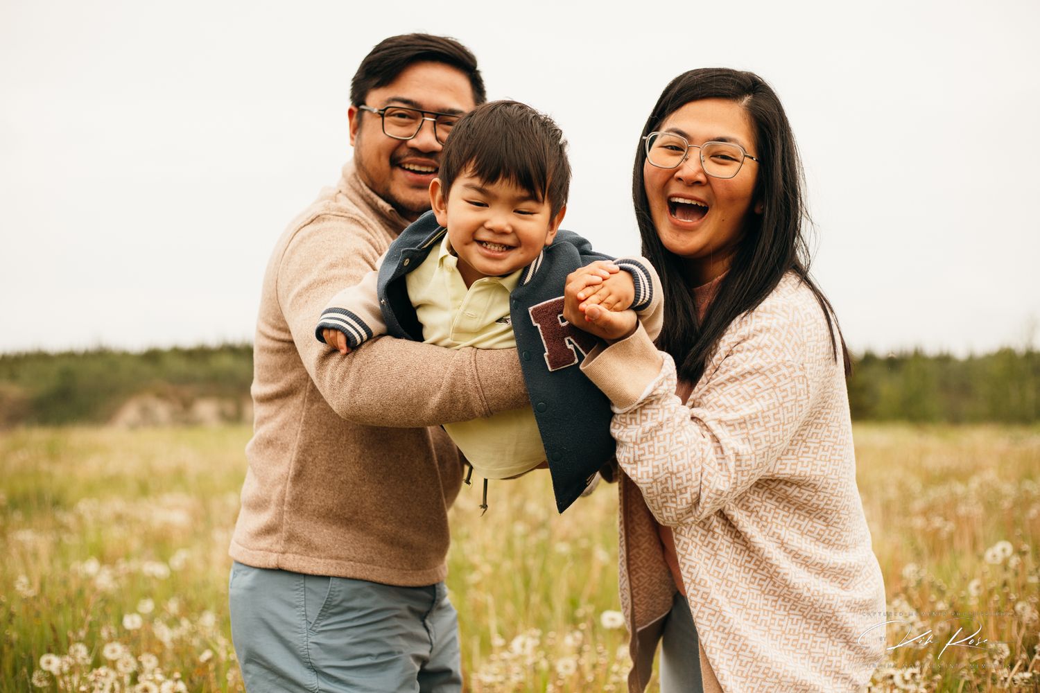 Happy Asian family with young child laughing together in a field of wildflowers.