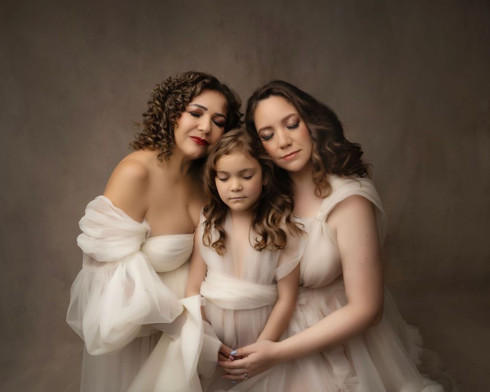 Three figures in ethereal white dresses pose together in soft studio lighting.
