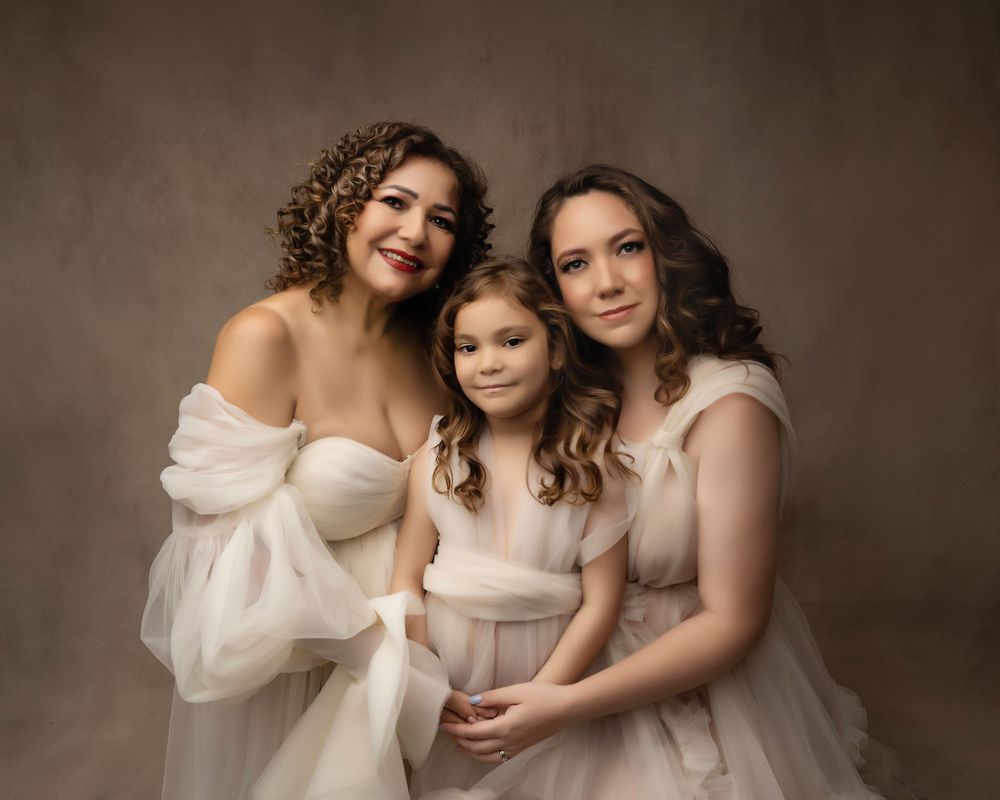 Studio portrait of three generations embracing in flowing white dresses.