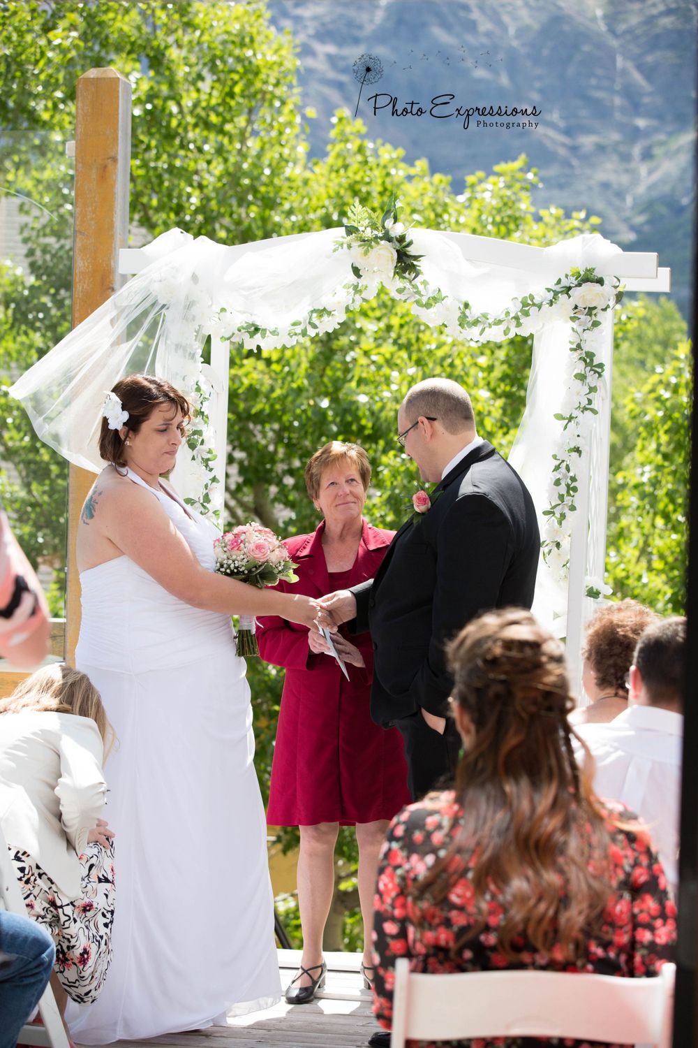 Outdoor wedding ceremony under white fabric arch with mountain backdrop.