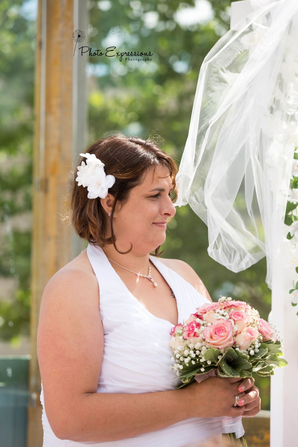 Person in white dress holding bouquet during outdoor ceremony.