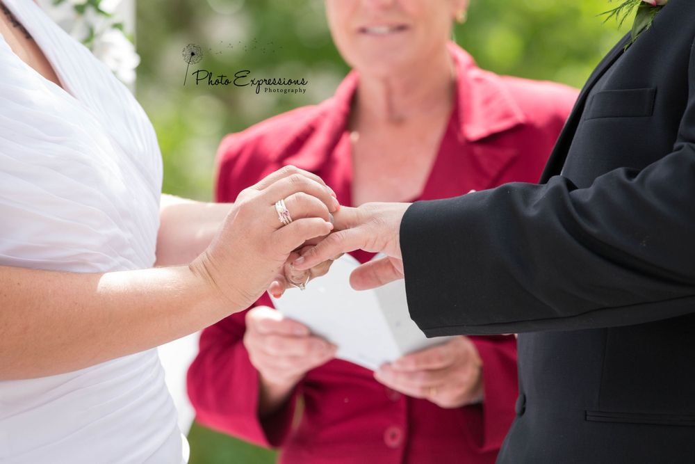 A couple exchanges rings during an outdoor wedding ceremony with a pink-clad officiant.