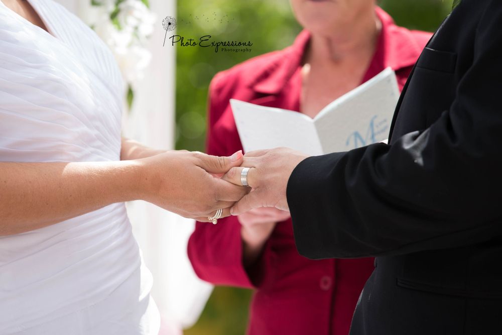 A couple exchanges rings during an outdoor wedding ceremony with a pink-clad officiant.