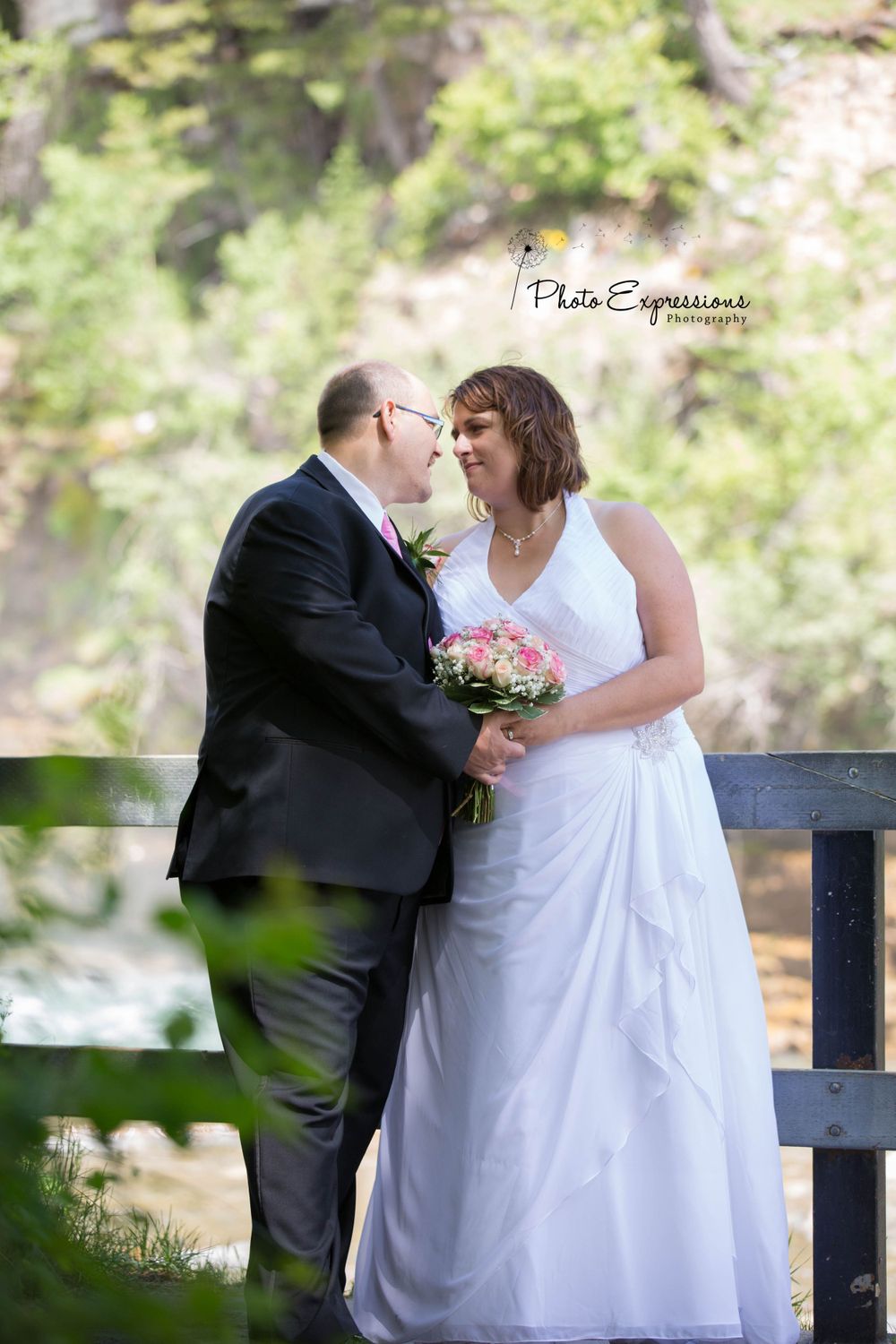A tender moment between newlyweds on a wooden bench outdoors.