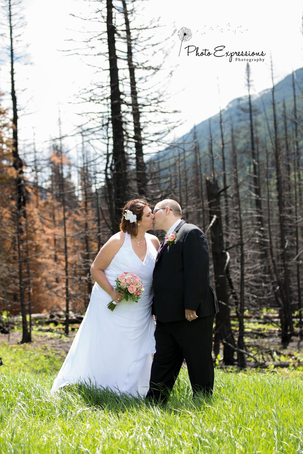 A wedding couple poses in a mountain meadow with burnt trees in the background.