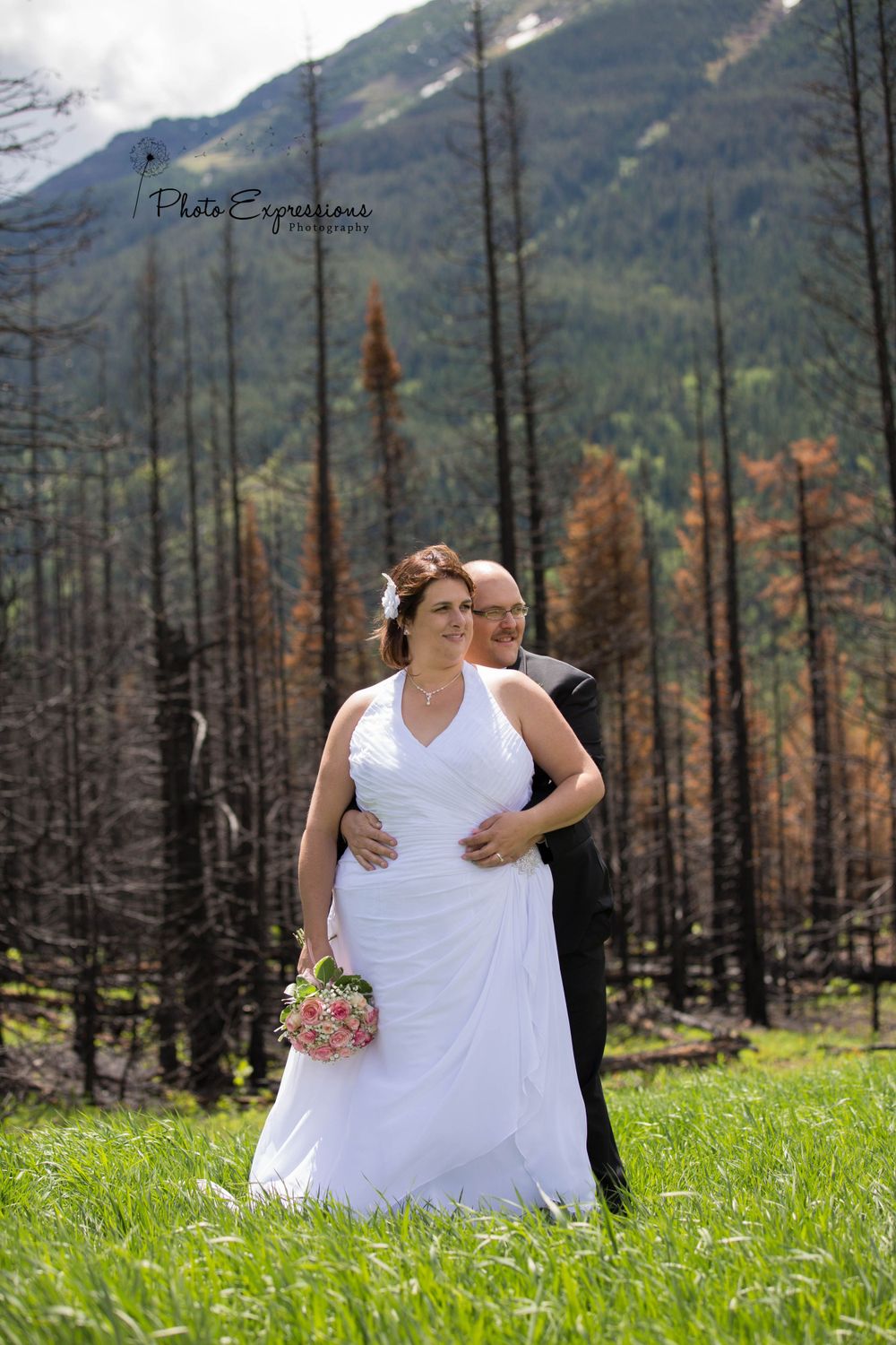 Newlyweds embrace in a mountain meadow with dramatic landscape views.