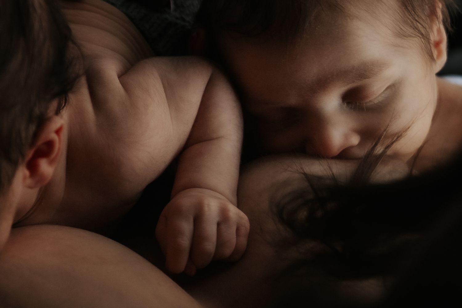 A mother and child in a tender embrace near a nursing rocking chair, captured in warm moody lighting.