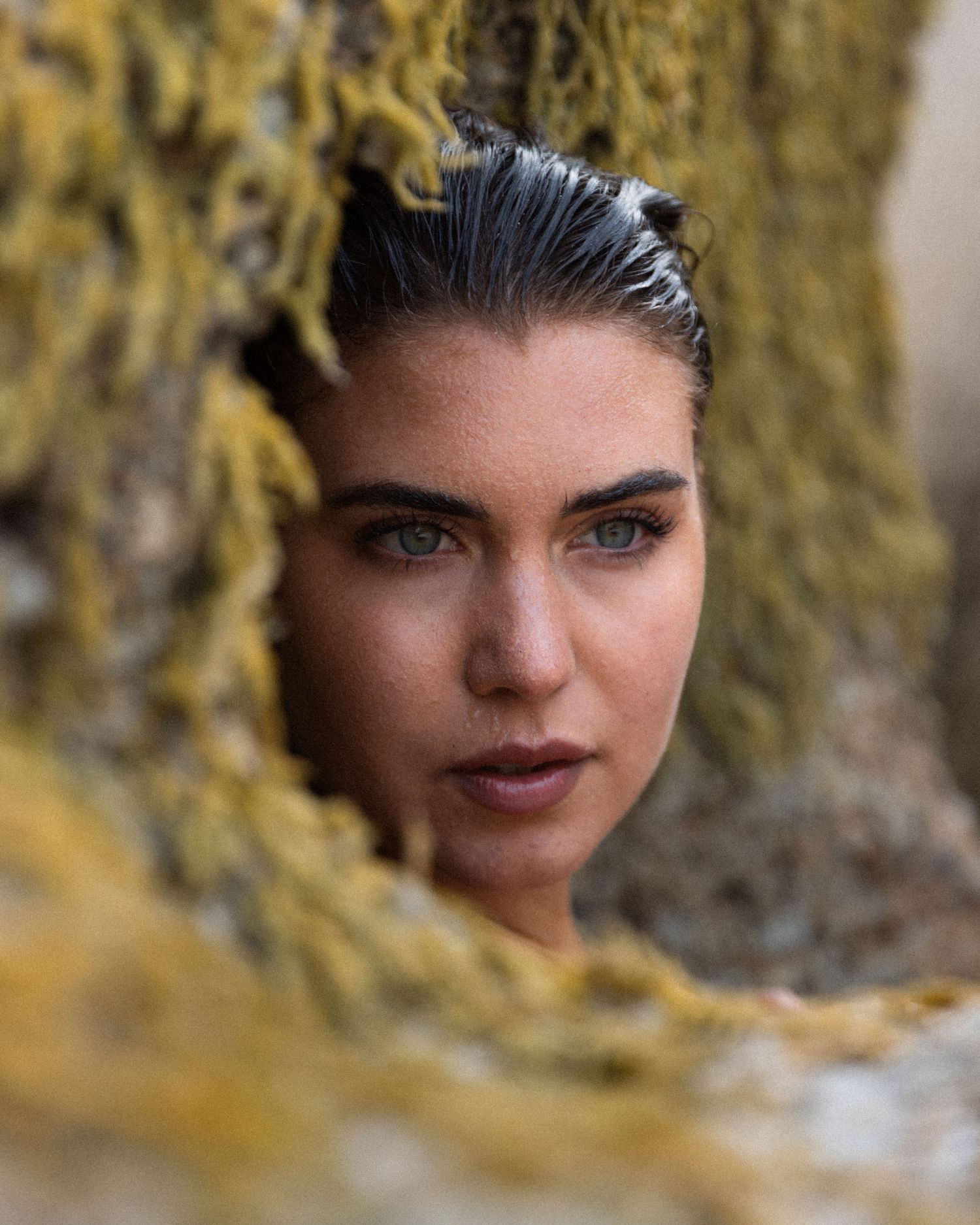 A close-up portrait framed by yellow foliage with wet styled hair.