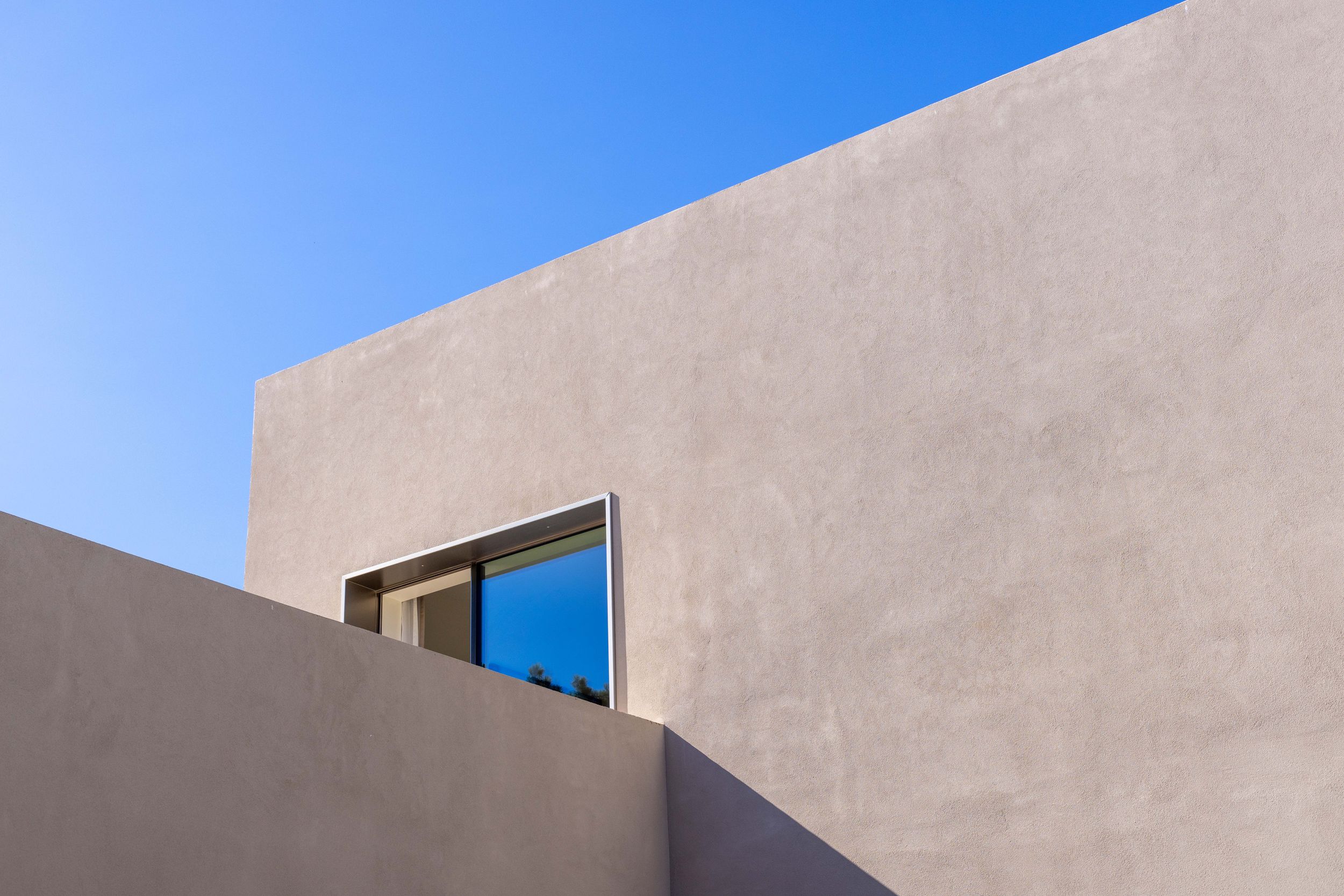 A modern adobe style house with white stucco walls and clean geometric lines stands against a bright blue sky.