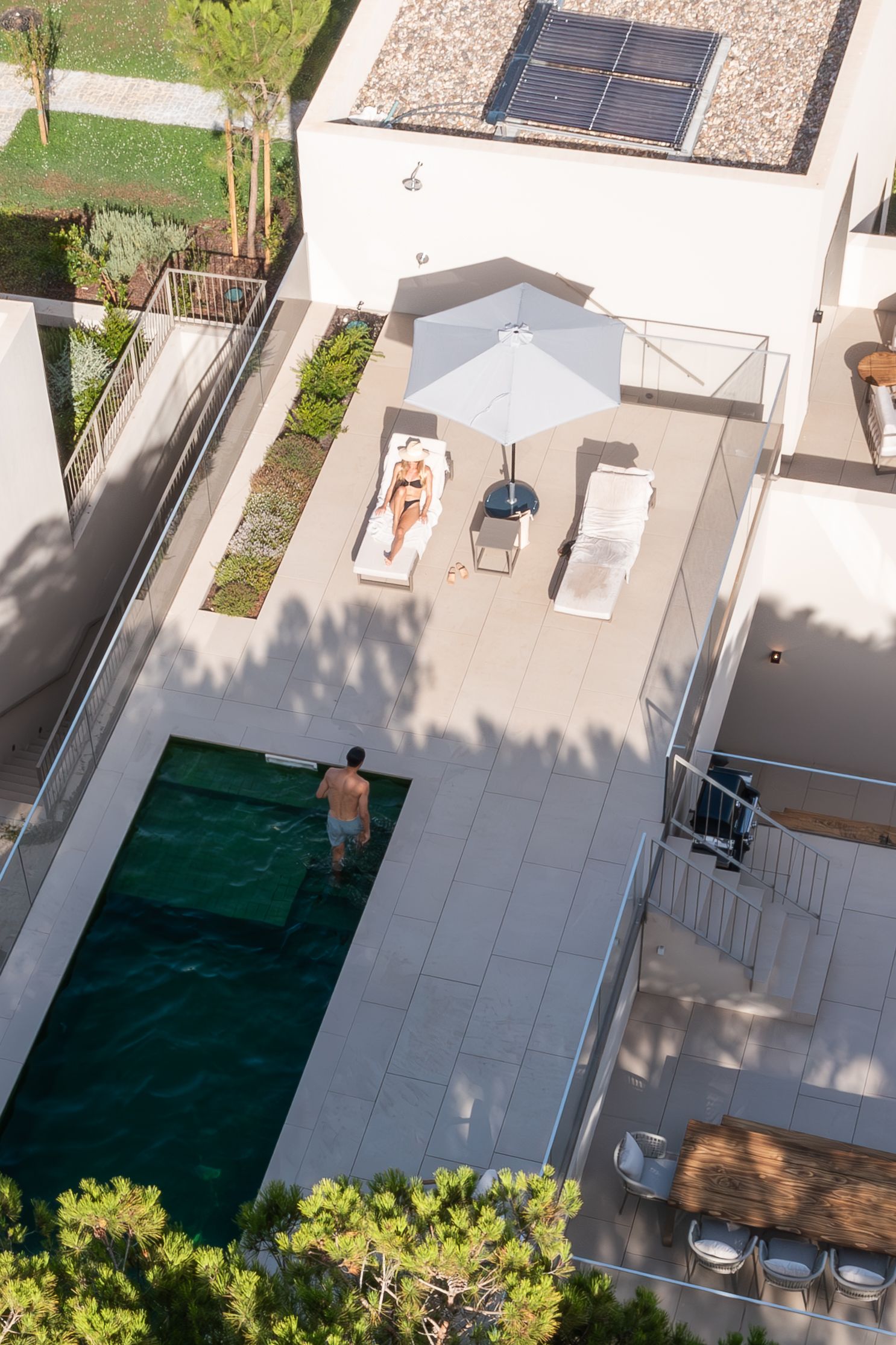 Aerial view of a private swimming pool and sunbathing area with lounge chairs and umbrella.