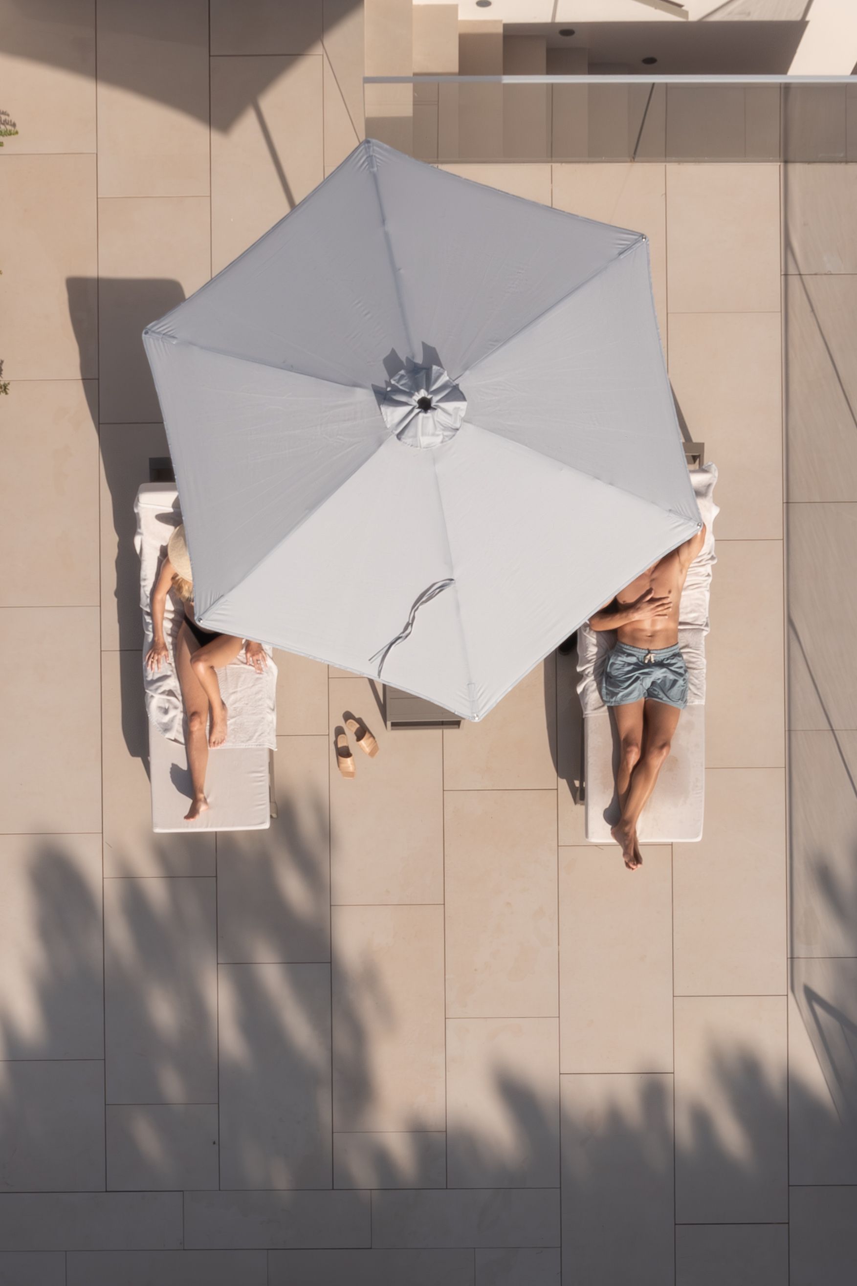 Top-down view of sun loungers under a grey umbrella on a resort patio.