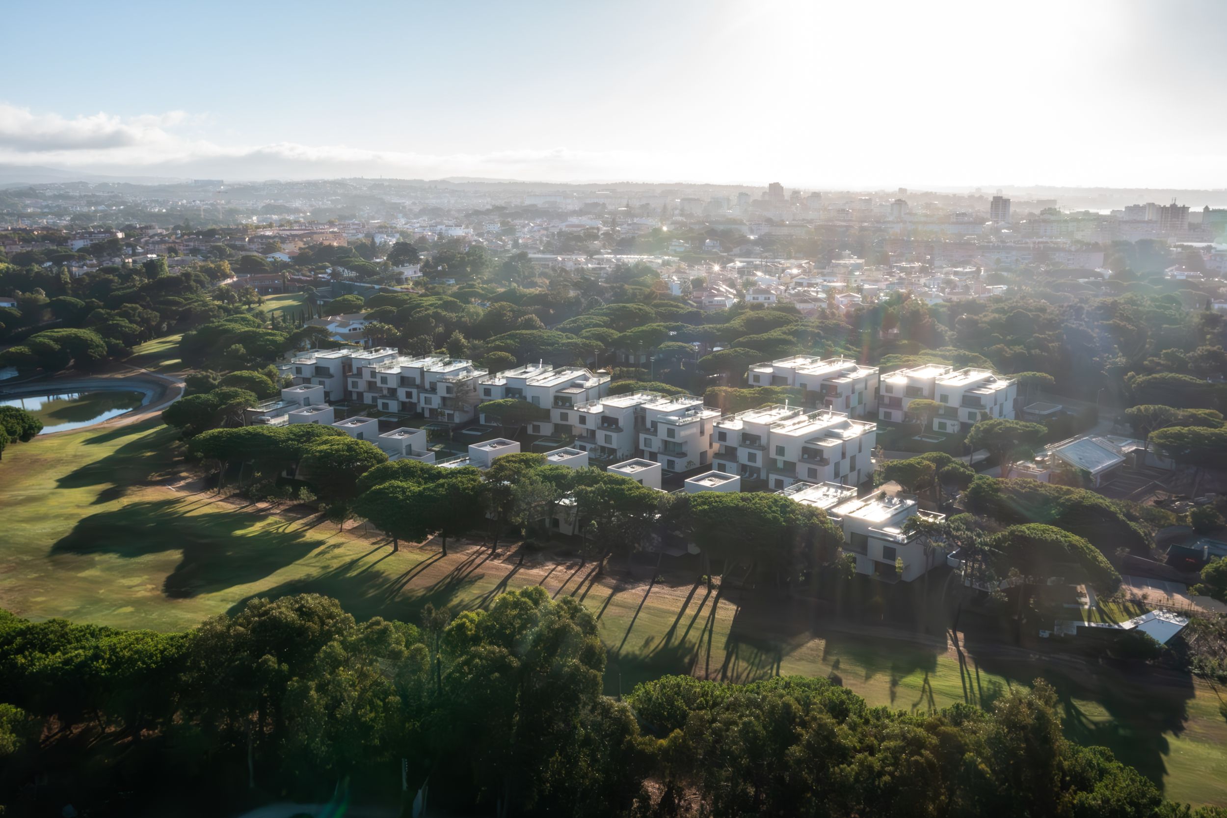 Aerial view of a coastal community with neat rows of white houses and green spaces under a hazy sky.