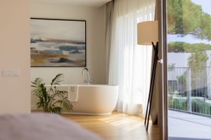 Modern bathroom interior with freestanding tub, artwork and sheer curtains letting in natural light.