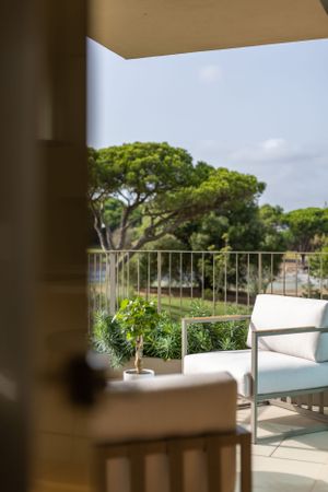 Luxury balcony view framed by doorway showing green trees and outdoor furniture.