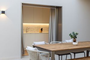 Contemporary dining area with wooden table and white chairs next to an illuminated kitchen space.